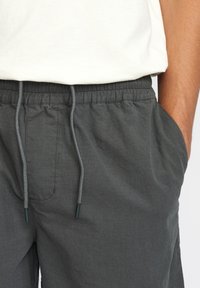 Grijze shorts met een elastische tailleband, verstelbaar trekkoord en zijzakken. De stof heeft een subtiele textuur en een kruissteekpatroon.