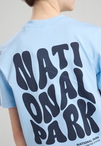 Light blue cotton t-shirt with a rounded neckline featuring large, rounded black lettering spelling "NATIONAL PARK" on the back.