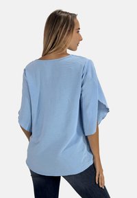 Lichtblauwe short-sleeve top met een ontspannen pasvorm, textuurstof en een ronde nek. Onderkant licht gebogen aan de achterkant voor een vloeiende uitstraling.