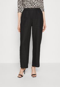 Zwarte linnen wijde broek met een gestructureerde afwerking, voorzien van voorzakken en een relaxte pasvorm, gecombineerd met zwarte sandalen met hoge hakken.