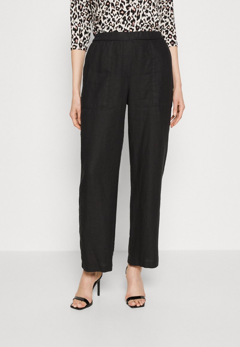 Zwarte linnen wijde broek met een gestructureerde afwerking, voorzien van voorzakken en een relaxte pasvorm, gecombineerd met zwarte sandalen met hoge hakken.