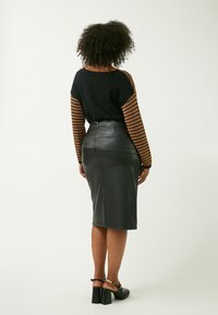 Schwarzer Pullover mit strukturierten braunen und schwarzen gestreiften Ärmeln, kombiniert mit einem figurbetonten schwarzen Leder-Midiskirt und klobigen schwarzen Absätzen.