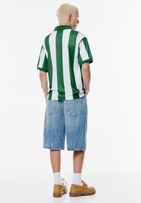 Groen-wit gestreepte polo shirt, relaxed fit; gecombineerd met lichtblauwe verouderde denim shorts. Schoeisel: tan, chunky-soled schoenen.