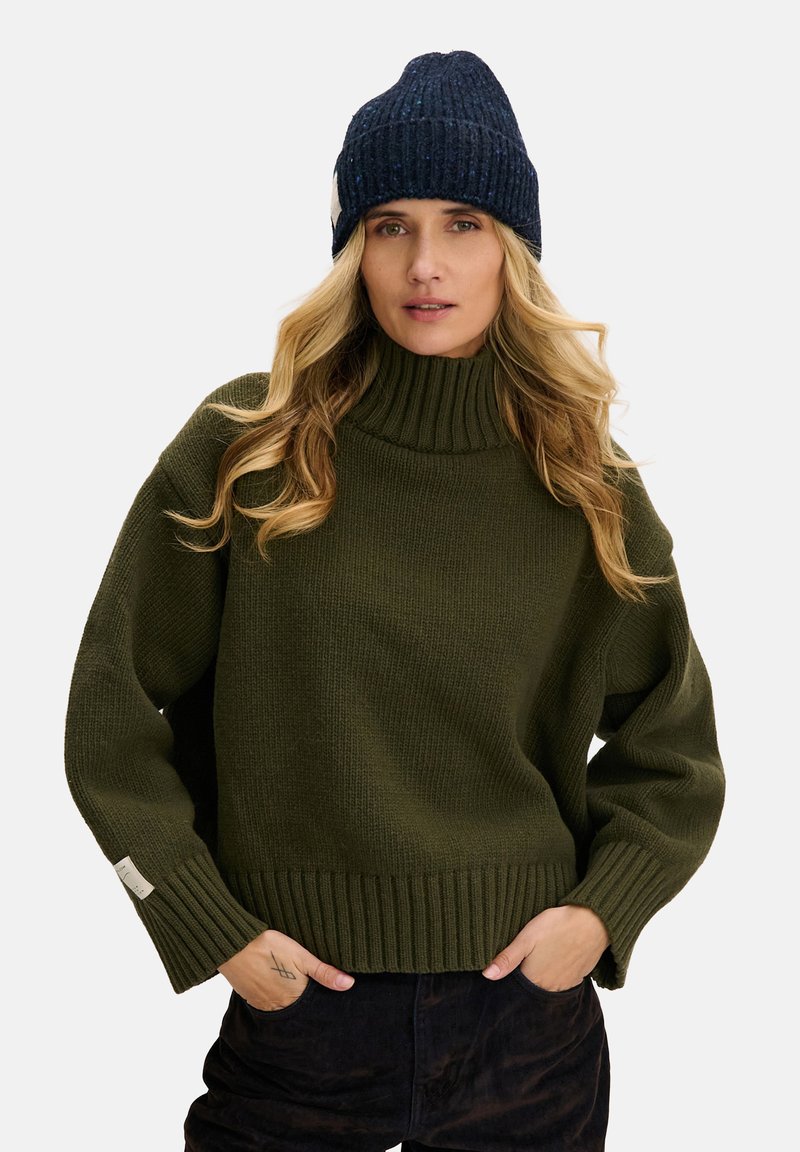 Zielony sweter z dzianiny z wysokim golfem i prążkowanym dołem. W połączeniu z granatową teksturowaną czapką typu beanie. Oba elementy garderoby mają luźny krój.