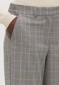 Pantaloni a quadri grigi e neri con una vestibilità su misura, caratterizzati da una texture liscia e tasche laterali. Il design affusolato completa il motivo.