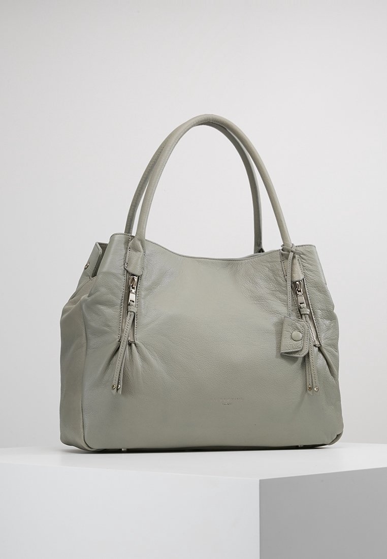 Szara skórzana torebka z dwoma bocznymi suwakami, zaokrąglonym wierzchem i krótkimi uchwytami. Posiada teksturowane wykończenie oraz małą dekoracyjną zawieszkę.