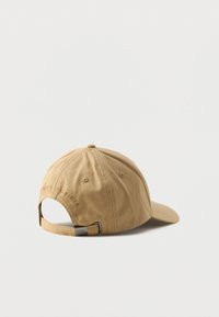 Cappellino da baseball beige regolabile con fibbia in metallo e testo ricamato "Tommy Hilfiger" sul retro, mostrato su uno sfondo bianco.