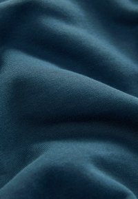 Tessuto verde scuro con una superficie liscia e morbida. Il materiale appare elastico con dettagli di tessitura sottili e uniformi.