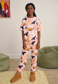 Twee-delig pyjama set met een roze basis en Halloween-thema patronen, waaronder skeletten, pompoenen en vleermuizen; zachte stof, relaxed fit.