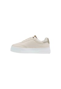 Zapatilla beige de corte bajo con suela blanca y gruesa, cordones delanteros y detalle metálico dorado en el cuello del talón, mostrada en perfil lateral.