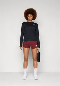 Juoda ilgomis rankovėmis sportinė marškinėliai, bordo spalvos šortai su baltu Nike logotipu, baltos kojinės ir sportbačiai. Laiko juodą gertuvę.