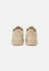 Beżowe sneakersy z zamszu i skóry o gładkim wykończeniu, z pomarańczowym logo na pięcie i grubą kremową podeszwą.