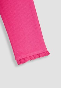 Tissu rose côtelé avec un détail de bord scallopé. La texture est lisse et le design est ajusté autour de la jambe.