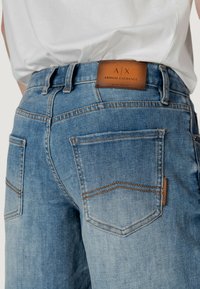 Jeans de mezclilla azul desgastados con cintura media, presentan una etiqueta de parche de cuero, costuras en contraste y dos bolsillos traseros.