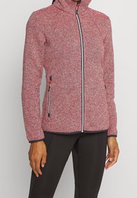 Veste zippée rayée rouge et blanc avec un col montant, tissu texturé, accents de fermeture éclair noirs, et poches latérales. Coupe ajustée près du corps.