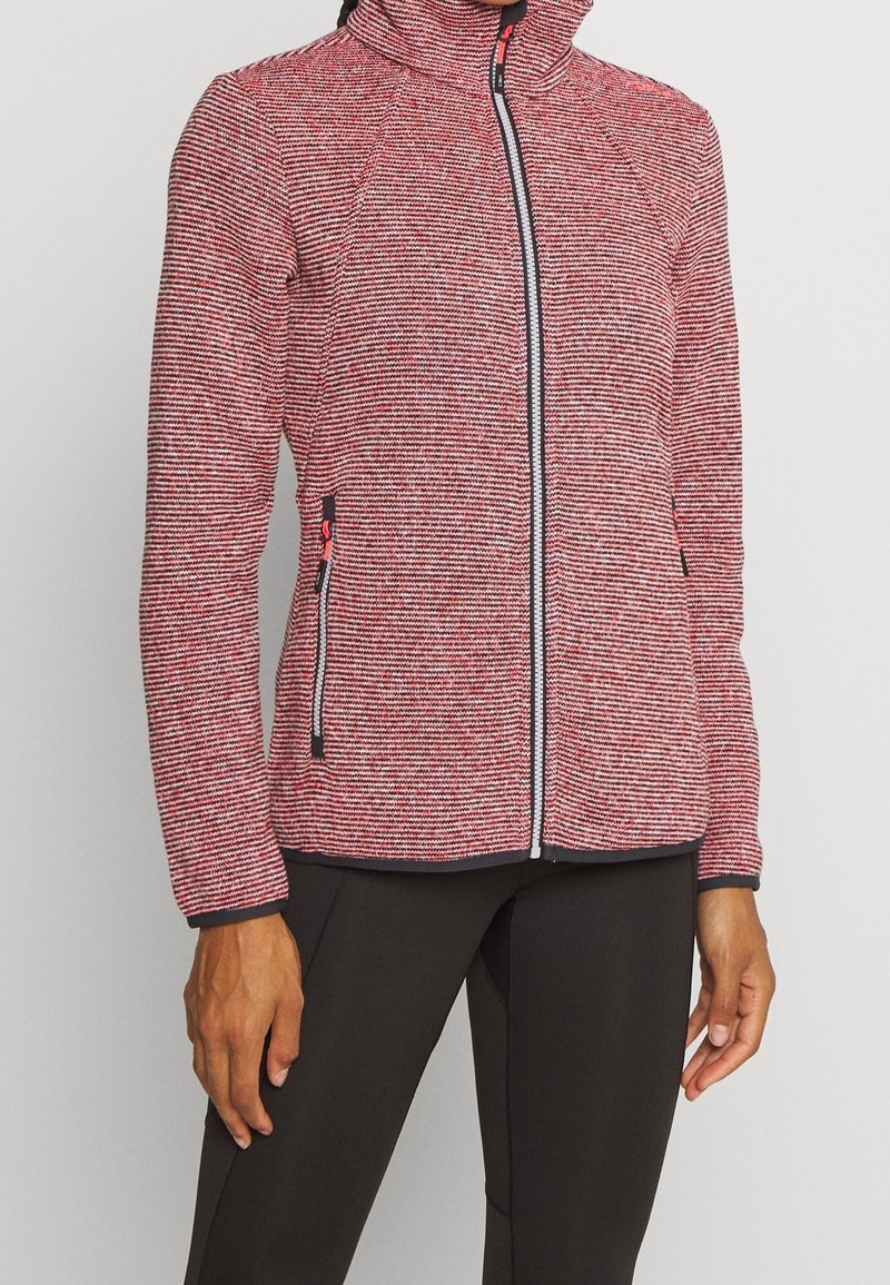 Veste zippée rayée rouge et blanc avec un col montant, tissu texturé, accents de fermeture éclair noirs, et poches latérales. Coupe ajustée près du corps.