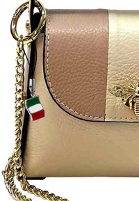 Sac à main en cuir tan et doré avec fermoir rabattable, bandoulière en chaîne dorée et emblème d'abeille. Il présente un petit charme en forme de drapeau italien.