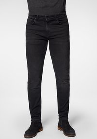 Svarta denimjeans med slim fit-design, femficksstil, subtila blekta områden och minimala sömnadsdetaljer. Kombineras med svarta ankelboots.