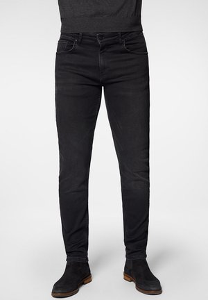 Vaqueros de mezclilla negros con un diseño ajustado, estilo de cinco bolsillos, áreas sutilmente descoloridas y un detalle de costura minimalista. Combinados con botas negras hasta el tobillo.