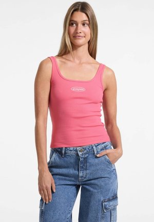 Top a coste rosa con scollatura quadrata e logo al centro, abbinato a pantaloni cargo in denim azzurro chiaro con tasche laterali.