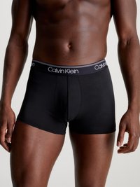 Schwarze Baumwoll-Boxershorts mit einem weichen elastischen Bund, auf dem "Calvin Klein" in weißer Schrift steht. Glatte Textur und eng anliegendes Design.