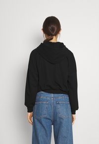 Felpa nera con cappuccio dal taglio rilassato, caratterizzata da un orlo a costine e dettagli sulla cucitura posteriore, abbinata a jeans chiari a vita alta.