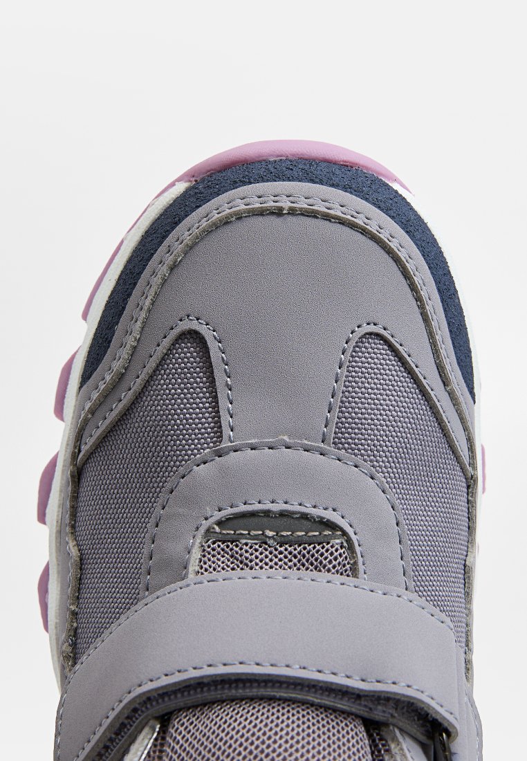 Szare buty sportowe z teksturowanej siateczki, z wyściółką złożoną z miękkiego materiału, oraz fioletową gumową podeszwą. Zapięcie na rzep zapewniające pewne dopasowanie.