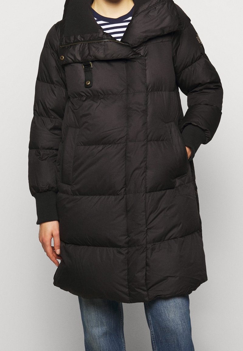 Svart pufferjacka med hög krage, horisontell quiltstruktur och framfickor. Har dragkedja och tryckknappsstängning. Texturerad tyg.