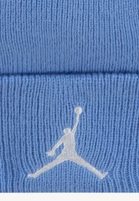 Světlomodrá pletená čepice s texturovanou tkaninou. Na přední straně se nachází bílé vyšívané logo Jumpman, které ukazuje sportovní design.