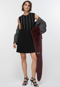 Top nero senza maniche con dettagli in perle, gonna nera plissettata, giacca grigia oversize e uno scialle di pelliccia sintetica color bordeaux. Sandali neri con cinturini.