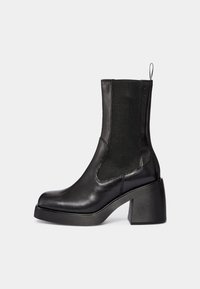 Czarny skórzany botek za kostkę z elastycznymi panelami po bokach, zaokrąglonym noskiem i masywnym obcasem. Gładka faktura, minimalistyczny design oraz pętelka do łatwego zakładania.
