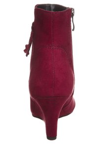 Bottine en daim bordeaux avec un talon incurvé, une fermeture éclair latérale et un nœud décoratif à l'arrière. Texture lisse et forme épurée.
