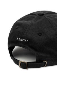 Musta farkkukotka, jossa on säädettävä hihna, valkoisella "KAOTIKO" brodeerauksella ja perinteisellä pyöreällä muodolla. Teksturoitu kangas ja vahvistetut saumat.