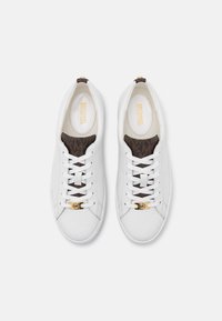 Sneakers in pelle bianca con una linguetta a pattern monogram marrone, lacci piatti e un accento in oro con logo sul lato. Texture liscia in tutto.