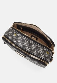 Geantă neagră cu fermoar, cu un model geometric în nuanțe de gri și alb. Are accesorii din aur, multiple compartimente și o căptușeală cu logo-ul brandului.