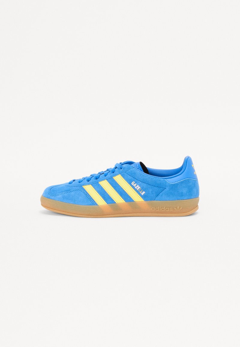 Blå ruskindsneakers med gule striber, gummisål og "Gazelle" branding. Runde tå og snørebåndsdesign.