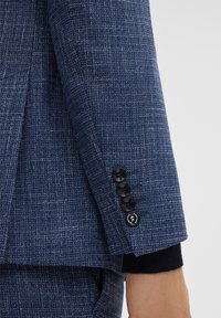 Manica di giacca navale in tessuto strutturato con un piccolo polsino in maglia e quattro bottoni neri, caratterizzata da un motivo sottile per un tocco di dettaglio in più.