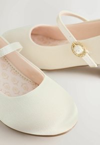 Balerini albi cu textură netedă, vârf larg și o curea decorativă cu o cataramă accentuată cu auriu. Căptușeală interioară roz.