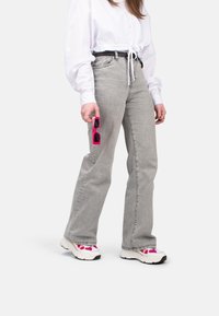 Jean gris évasé, en denim de poids moyen, taille haute, associé à un T-shirt court blanc. Tient des lunettes de soleil rectangulaires roses.