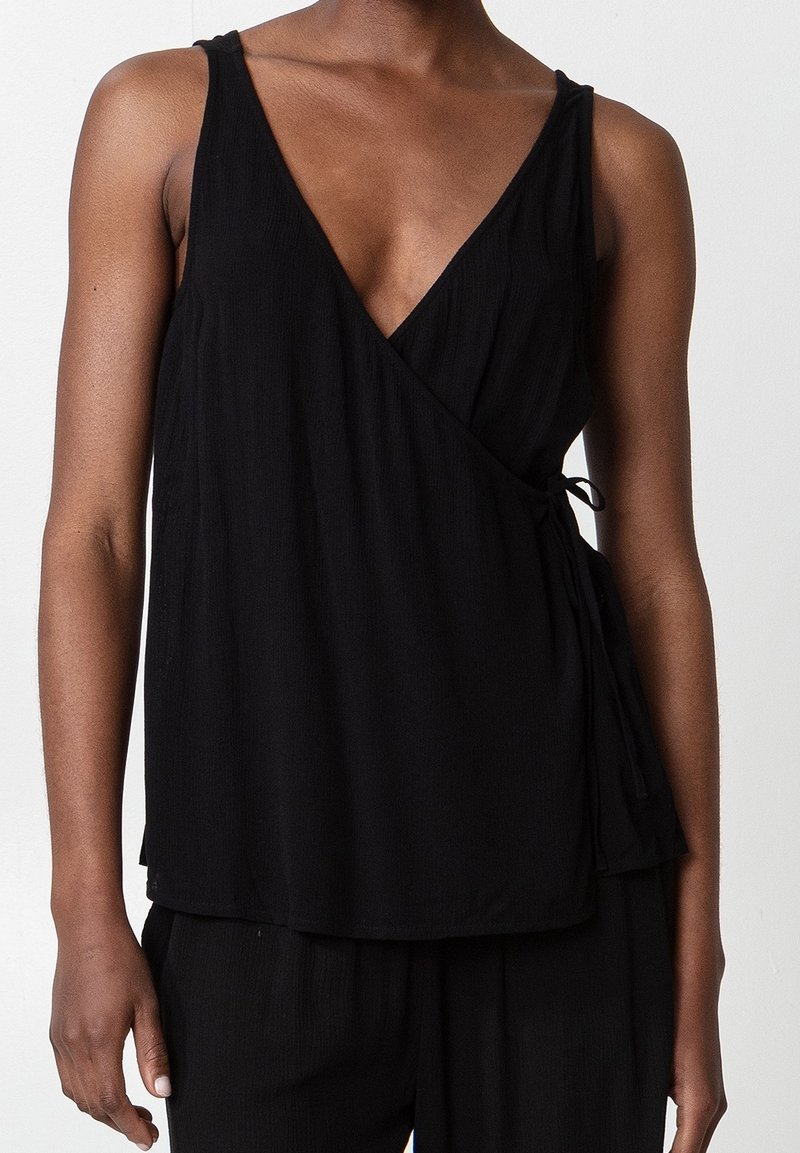 Top nero avvolgente con scollatura profonda a V, lacci regolabili in vita e tessuto leggero e texturizzato. Design senza maniche e vestibilità rilassata.