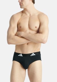 Schwarze Slips mit einer enganliegenden Passform, ausgestattet mit einem schwarzen Bund mit drei weißen Streifen und einem glatten, dehnbarem Stoff.