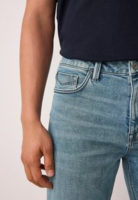 Világoskék farmernadrág, testhezálló szabással, enyhe kopott hatással és ötpántos zsebviselettel. Látható fém gomb és cipzáras záródás.