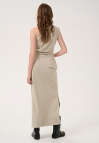 Beige two-piece outfit featuring a sleeveless draped top and a long skirt with a side slit, paired with black ankle boots. Smooth texture.