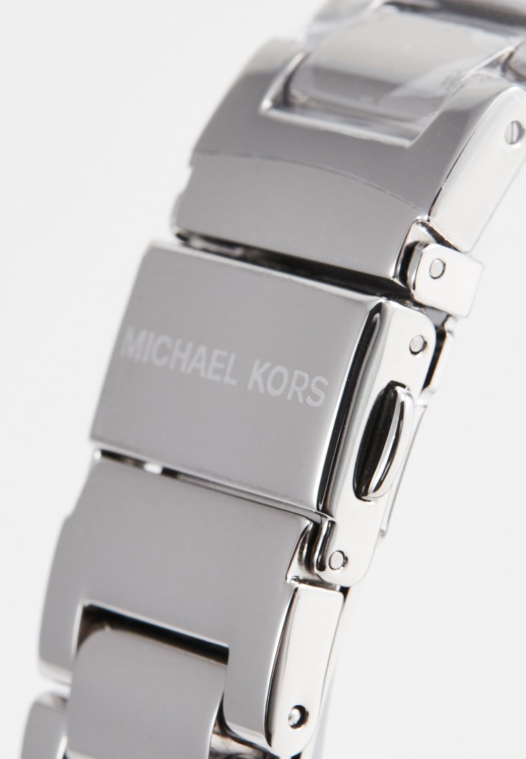 Roestvrijstalen horlogeband met gepolijste schakels, met gegraveerde tekst "MICHAEL KORS". Glad, glanzend oppervlak met een geometrisch ontwerp.