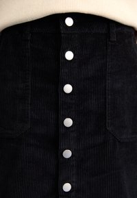 Jupe en velours côtelé noir avec une coupe droite, fermeture à boutons à l'avant avec quincaillerie en argent et tissu texturé à côtes.