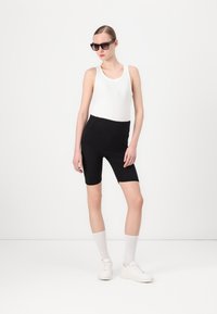 Zwarte fietsshorts met een hoge taille, gecombineerd met een witte tanktop, witte sneakers en zwarte zonnebril. Glad materiaal, strakke pasvorm.