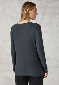 Waffelstrukturierter, langärmeliger Pullover in Dunkelgrau mit rundem Ausschnitt und leicht verlängertem Rücken. Weicher Stoff, lockere Passform.