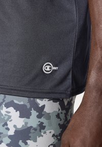 Crna atletska majica s "DRY" logotipom, u kombinaciji s tajicama u sivo-plavom kamuflažnom uzorku. Majica ima glatku teksturu i prilagođen dizajn.