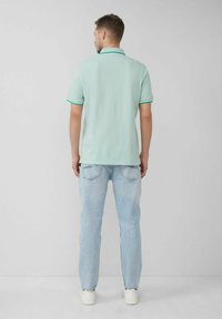 Mintgrünes Polohemd mit kontrastierendem türkisem Besatz, kombiniert mit hellblauen Jeans und weißen Sneakers, von hinten betrachtet.