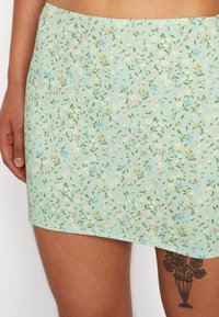Saia mini verde menta com um padrão floral em rosa, amarelo e azul, feita de tecido leve, com uma textura suave e cós elástico.